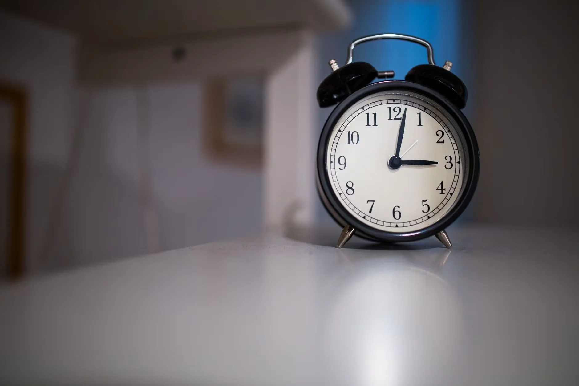 A classic black alarm clock with a white face showing 7:05, placed on a white surface.