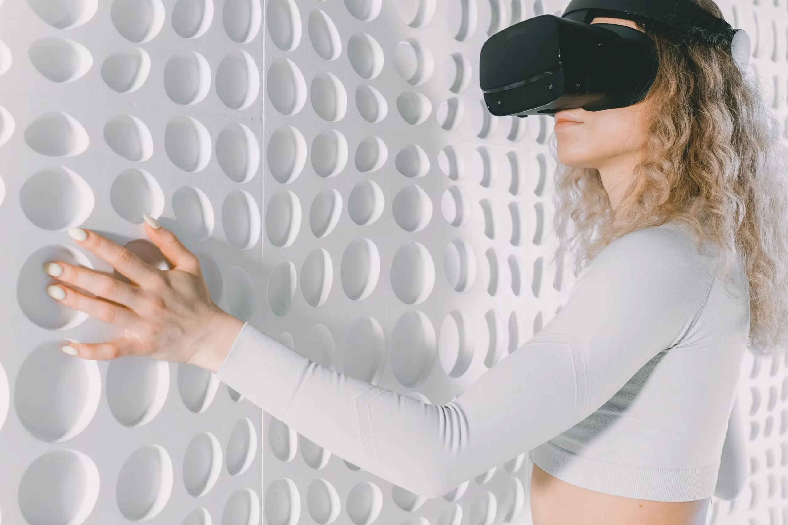 Woman explores a white textured wall using virtual reality headset, capturing advanced tech and tactile perception.